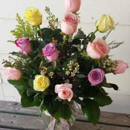 Mixed pastel roses arranged in a clear glass vase with a ribbon