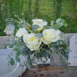White roses in a clear glass vase with eucalyptus greenery