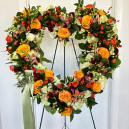 Heart-shaped floral wreath with orange roses and mixed blooms on a stand
