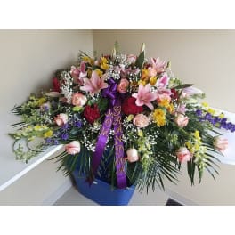 Large mixed floral spray in a blue container with purple ribbons