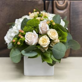 White roses and green pom-pom flowers in a white square vase