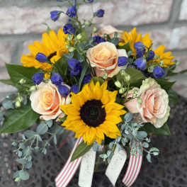 Bouquet of sunflowers, peach roses, and blue bellflowers with ribbon tails