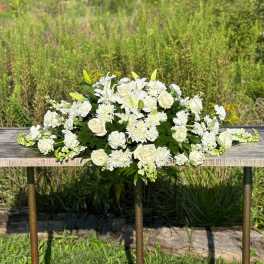 Long all-white arrangement of lilies, roses, and mums on a rustic wooden table outdoors