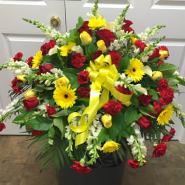 Large red and yellow floral arrangement with a yellow ribbon in a black container