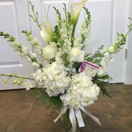 White floral arrangement with calla lilies, roses, and hydrangeas in a glass vase