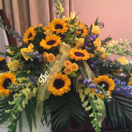 Large funeral spray with sunflowers, yellow roses, and purple flowers