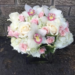 White and pink bouquet with roses, orchids, and hydrangeas in a black vase