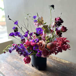 Mixed bouquet of purple, pink, and burgundy flowers in a black vase