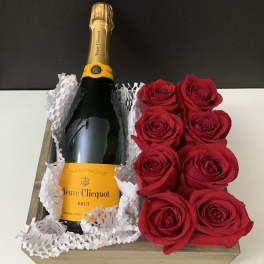 Champagne bottle in a wooden gift box beside red roses