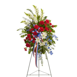 Standing floral spray with red carnations, white lilies, and blue accents on an easel