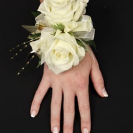 Wrist corsage of ivory roses with ribbon accents worn on a hand against a black background.