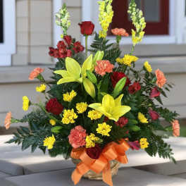 Mixed bouquet with yellow lilies, red roses, and carnations in a basket with orange ribbon