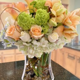 Peach and white roses, lilies, and hydrangeas in a clear glass vase with river stones