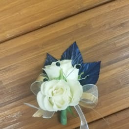 Small white rose corsage with dark blue leaves and ribbon on a wooden surface