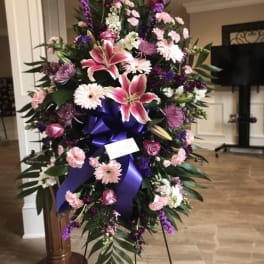 Large standing floral spray with pink lilies and purple flowers on a ribboned easel