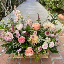 Low floral arrangement with pink, peach, and lavender blooms in a wooden container