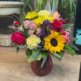 Mixed bouquet with sunflowers, roses, carnations, and alstroemeria in a red vase