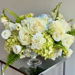 White roses and pale blue hydrangeas in a clear glass vase