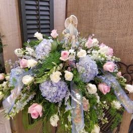 Large pastel floral spray with roses and hydrangeas around a religious figurine