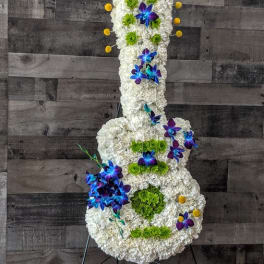 Tall guitar-shaped floral arrangement in white with blue orchids and green accents on a metal stand