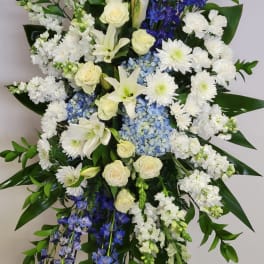 Tall white and blue standing spray with lilies, roses, hydrangeas, and mums on a metal easel