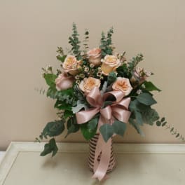 Peach roses in a striped vase with a pink ribbon bow