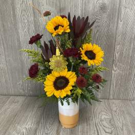 Sunflowers and burgundy carnations in a white and orange vase