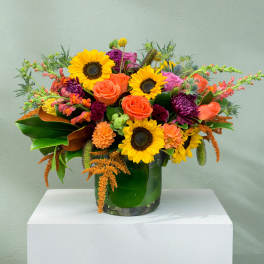 Bright mixed bouquet with sunflowers, roses, and purple blooms in a glass vase