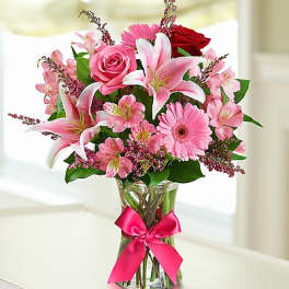 Pink and red flower bouquet in a glass vase with a pink ribbon