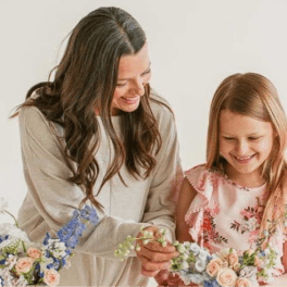 Woman and young girl smiling while arranging pastel flowers together