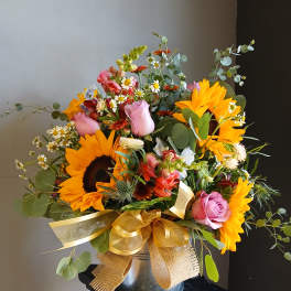 Mixed bouquet with sunflowers, pink roses, and daisies in a metal bucket