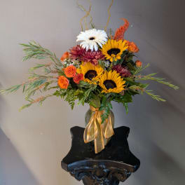 Mixed bouquet of sunflowers, gerbera daisies, and orange roses in a glass vase