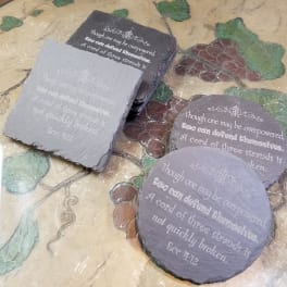 Four engraved slate coasters with a Bible verse on a decorative table.