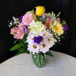 Mixed bouquet of roses, daisies, and gerbera daisies in a glass vase