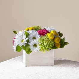 Mixed bouquet of white, yellow, and pink flowers in a white box