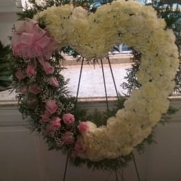 Heart-shaped floral wreath with white blooms and pink roses on an easel