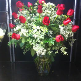 Red roses arranged in a clear glass vase with white filler flowers