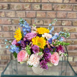 Mixed bouquet of pink, purple, blue, and yellow flowers in a white vase