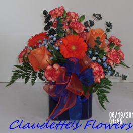 Orange and red flower arrangement in a dark vase with ribbon