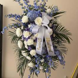 Standing floral spray with white roses, blue flowers, and a white ribbon