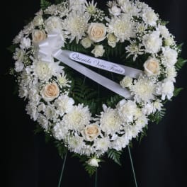 Heart-shaped white floral wreath on a stand with a ribbon bow