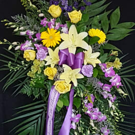 Standing floral spray with yellow roses, lilies, and purple flowers on a black background