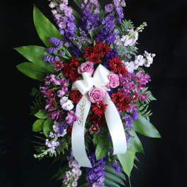 Tall standing floral spray with purple, pink, and red flowers and a white ribbon