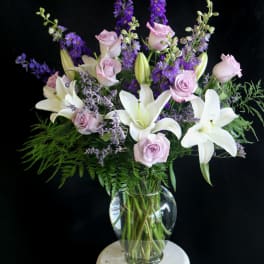 Bouquet of white lilies, pale pink roses, and purple flowers in a glass vase