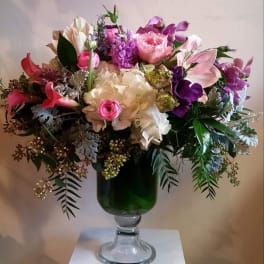 Mixed pink and purple flower arrangement in a green glass vase