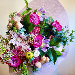 Bouquet of pink roses, lavender flowers, and mixed blooms wrapped in pale paper