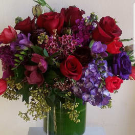 Red roses and purple flowers arranged in a green glass vase