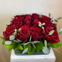 Red roses arranged in a low rectangular vase with green foliage