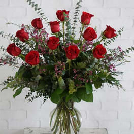 Red roses arranged in a clear glass vase with eucalyptus and filler flowers