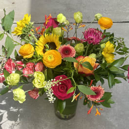 Mixed bouquet in a glass vase with sunflowers, roses, and bright pink blooms